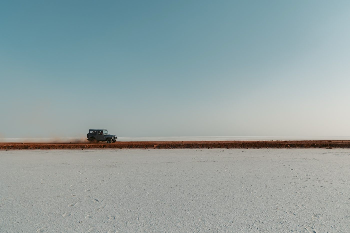 Jeep driving along a red-earth track beside the white salt flats of Kutch